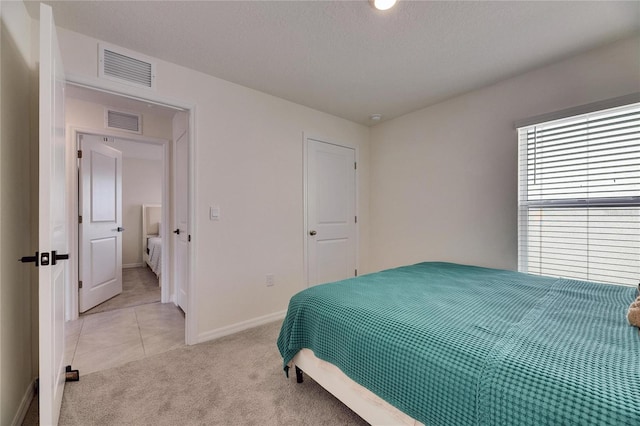 bedroom with baseboards, light tile patterned floors, visible vents, and light colored carpet