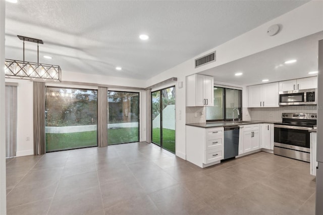 kitchen with pendant lighting, dark countertops, visible vents, appliances with stainless steel finishes, and white cabinetry