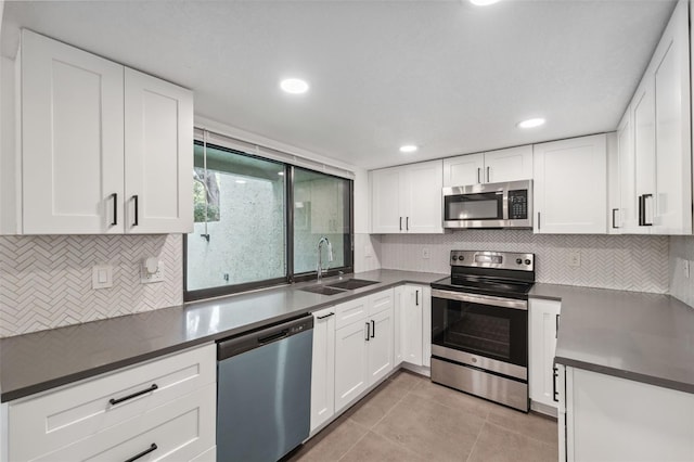 kitchen with dark countertops, appliances with stainless steel finishes, white cabinets, and a sink