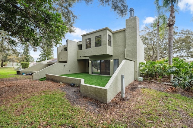 back of property featuring a lawn, a chimney, and stucco siding