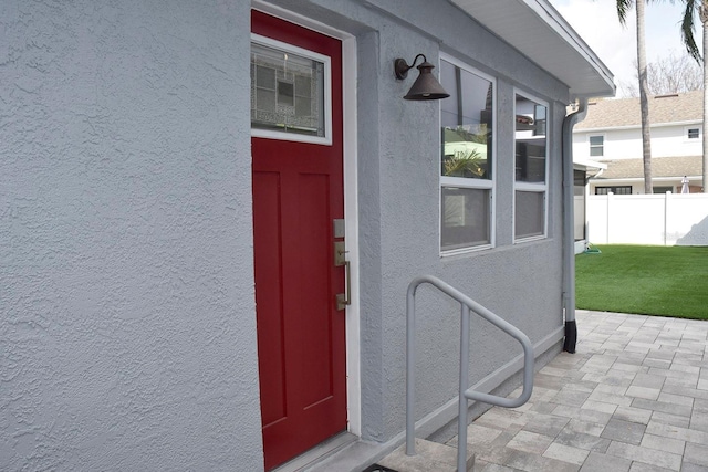 doorway to property featuring fence, a lawn, and stucco siding
