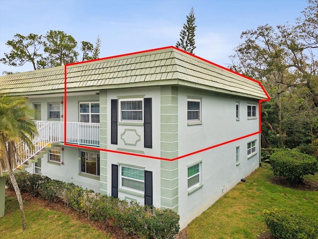 view of property exterior featuring stucco siding, a yard, and mansard roof