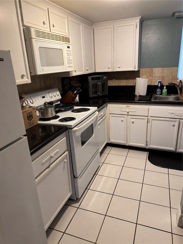 kitchen with white appliances, light tile patterned flooring, a sink, white cabinetry, and dark countertops