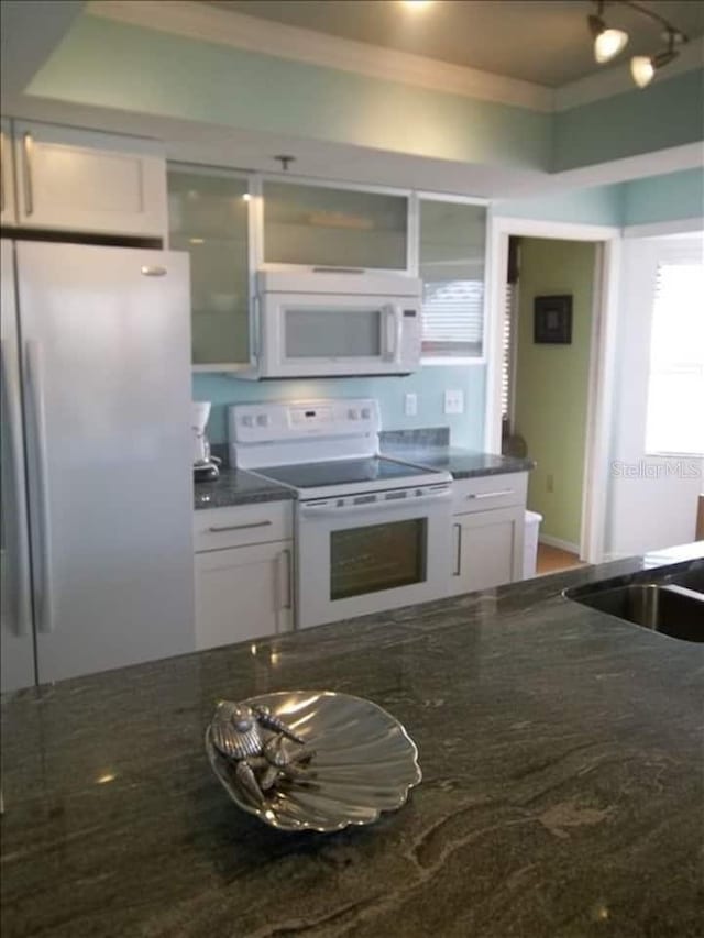 kitchen featuring white appliances, white cabinets, ornamental molding, sink, and dark stone countertops