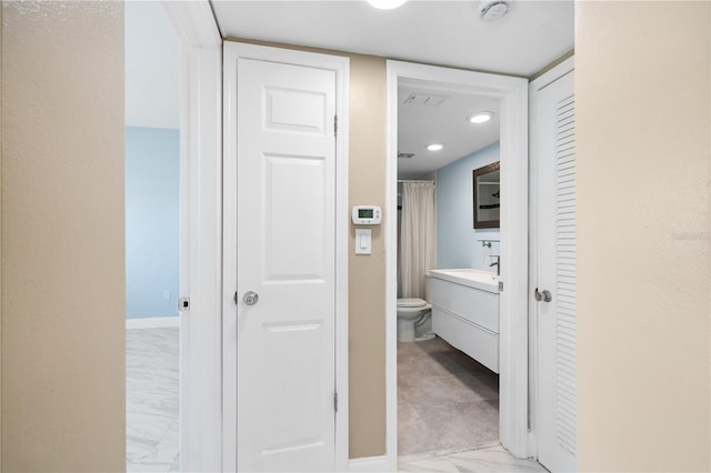 hall with marble finish floor, a sink, and baseboards