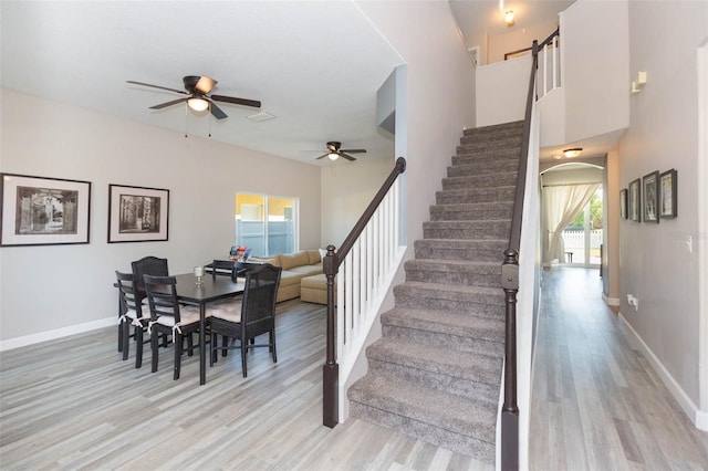 stairs featuring wood finished floors, a ceiling fan, baseboards, and arched walkways