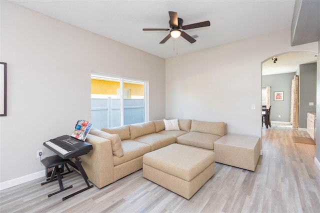 living area featuring arched walkways, baseboards, light wood-type flooring, and ceiling fan