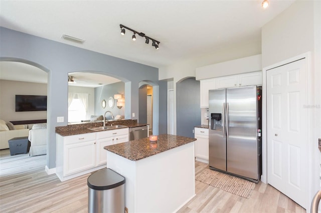 kitchen featuring a sink, dark stone counters, light wood finished floors, and stainless steel appliances