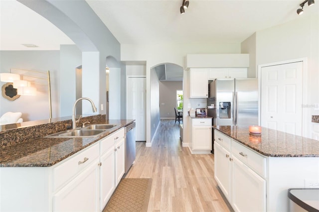 kitchen with light wood finished floors, a kitchen island, arched walkways, a sink, and appliances with stainless steel finishes