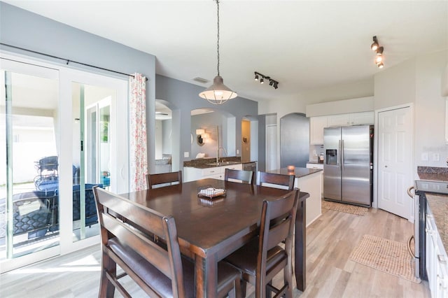 dining room featuring track lighting, arched walkways, and light wood-type flooring