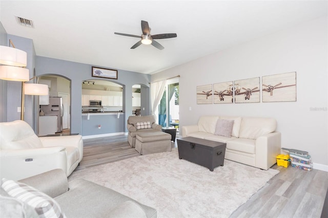 living area featuring visible vents, baseboards, wood finished floors, arched walkways, and a ceiling fan