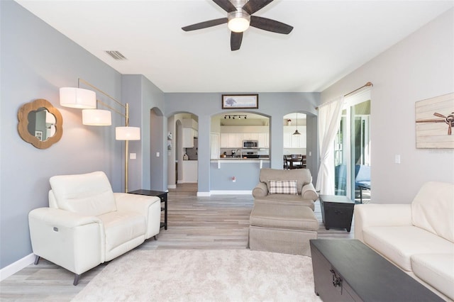 living room featuring visible vents, a ceiling fan, arched walkways, light wood-style floors, and baseboards