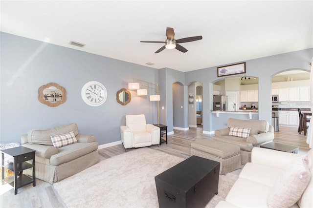 living area featuring baseboards, a ceiling fan, arched walkways, and light wood-type flooring