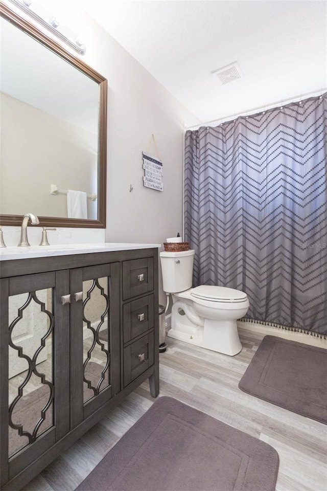 full bath with vanity, a shower with curtain, wood finished floors, visible vents, and toilet