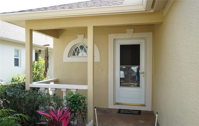 doorway to property featuring stucco siding and a shingled roof