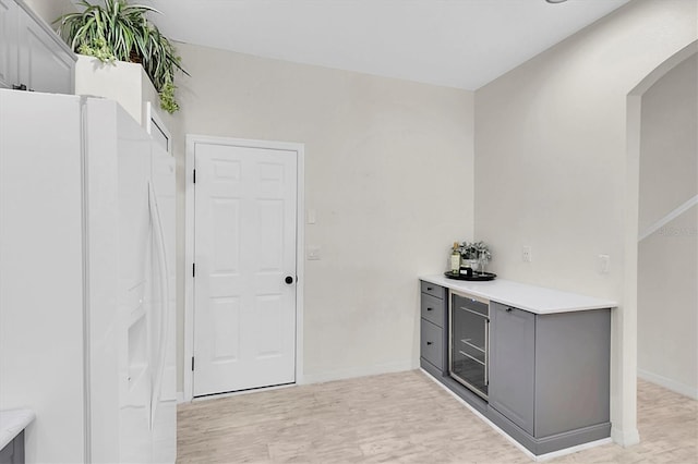 bar featuring light wood finished floors, white fridge with ice dispenser, baseboards, and arched walkways