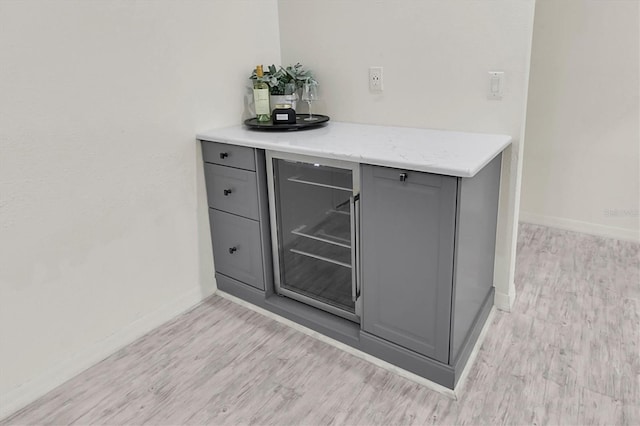 bar featuring beverage cooler, baseboards, and light wood finished floors