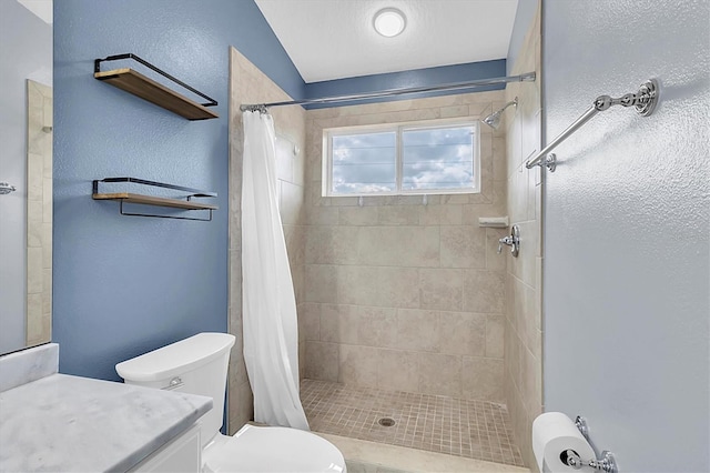 bathroom featuring a tile shower, a textured wall, vanity, and toilet