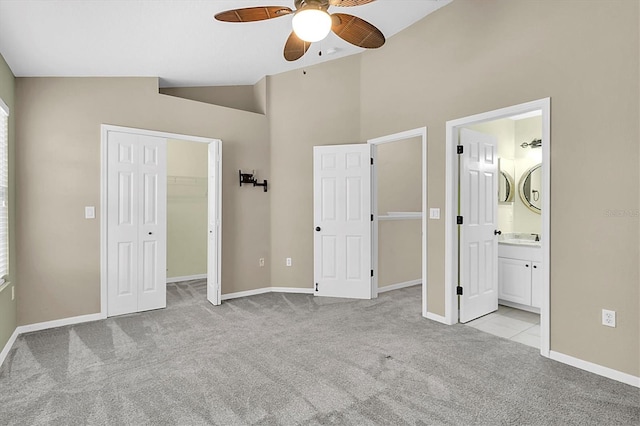unfurnished bedroom with lofted ceiling, light colored carpet, baseboards, a spacious closet, and ensuite bath