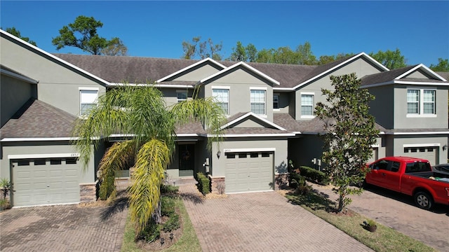 multi unit property with a garage, roof with shingles, driveway, and stucco siding