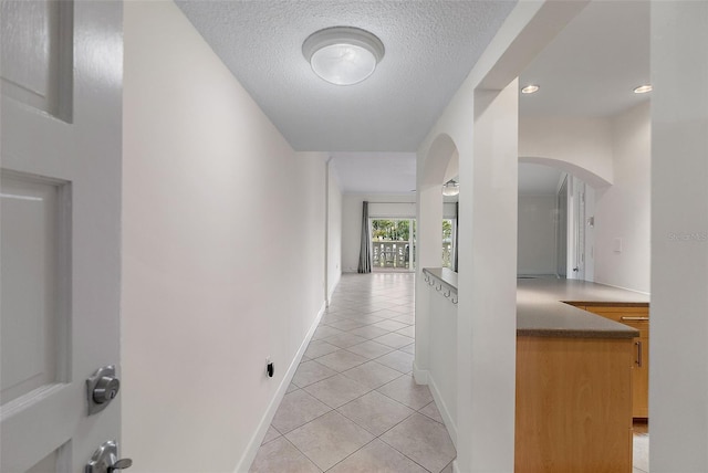 hallway with baseboards, arched walkways, a textured ceiling, and light tile patterned flooring