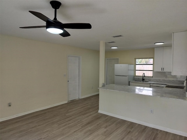 kitchen featuring white appliances, light countertops, light wood-type flooring, white cabinetry, and a sink