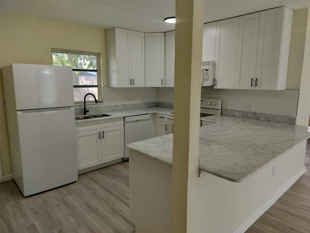 kitchen with light wood-style flooring, a peninsula, white appliances, a sink, and white cabinets