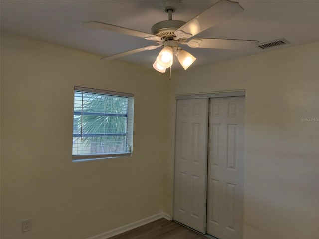 unfurnished bedroom featuring wood finished floors, a ceiling fan, visible vents, baseboards, and a closet