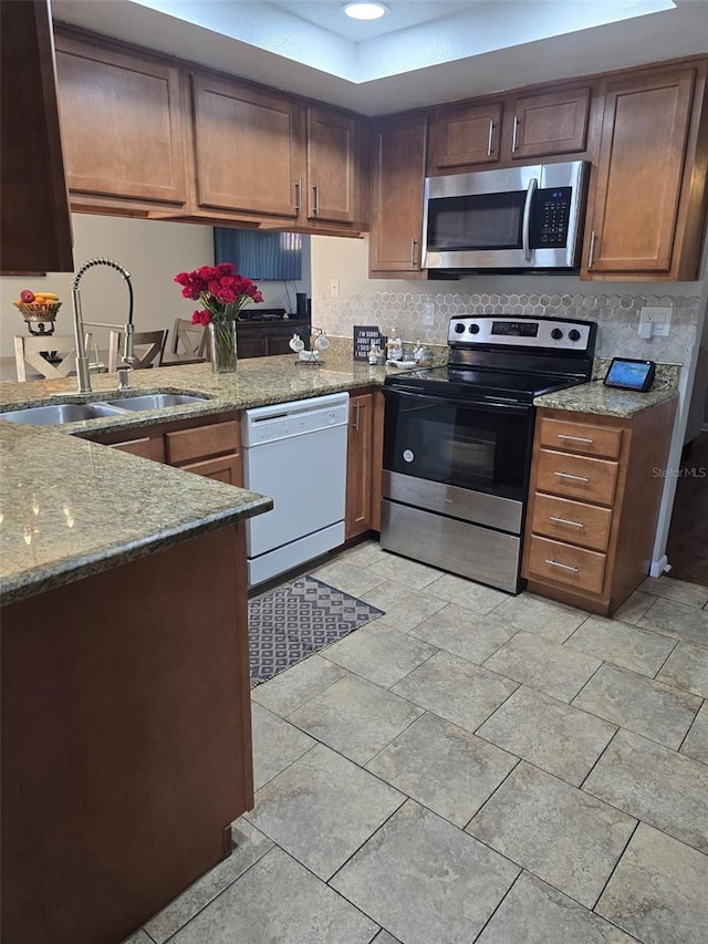 kitchen with appliances with stainless steel finishes, sink, stone countertops, and kitchen peninsula