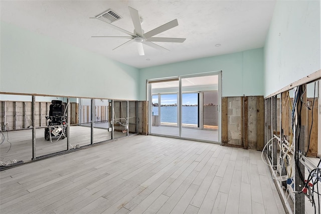 empty room featuring a water view, light hardwood / wood-style flooring, and ceiling fan