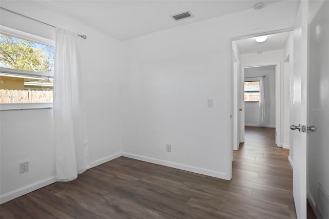 unfurnished room with dark wood-type flooring, visible vents, and baseboards