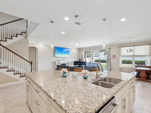 kitchen with light stone counters, a sink, open floor plan, an island with sink, and pendant lighting