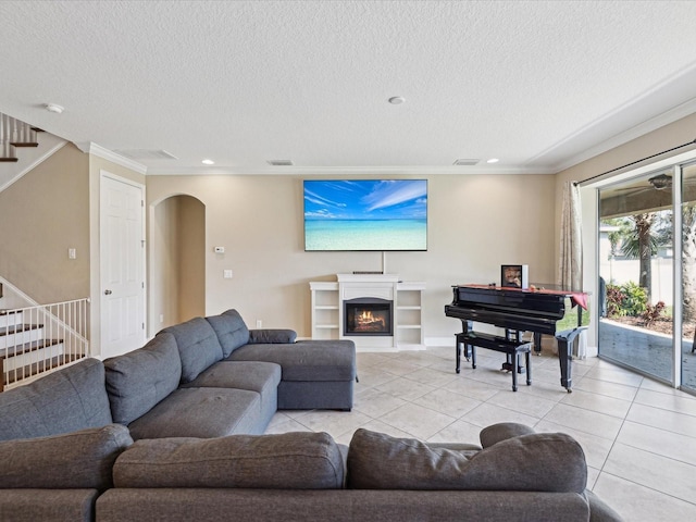 living room featuring arched walkways, crown molding, light tile patterned floors, a lit fireplace, and stairs