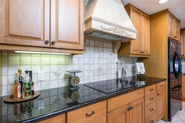 kitchen featuring premium range hood, dark stone counters, black appliances, backsplash, and light tile patterned floors