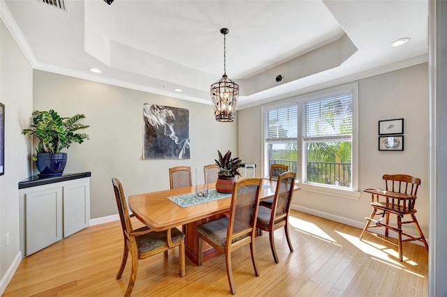 dining room featuring ornamental molding, a raised ceiling, baseboards, and light wood finished floors