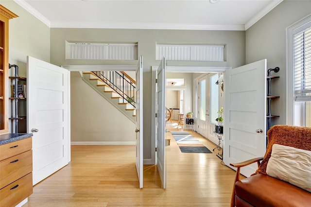 foyer featuring light wood finished floors, ornamental molding, stairs, and a wealth of natural light