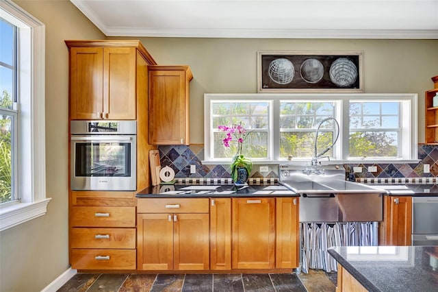 kitchen with stainless steel appliances, dark countertops, brown cabinets, and crown molding