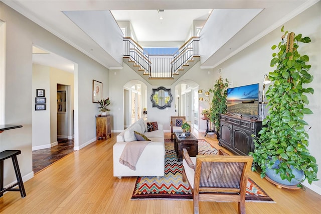 living area featuring arched walkways, a high ceiling, baseboards, ornamental molding, and light wood finished floors