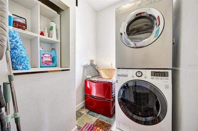 laundry room with stacked washer and dryer, laundry area, baseboards, and stone tile floors