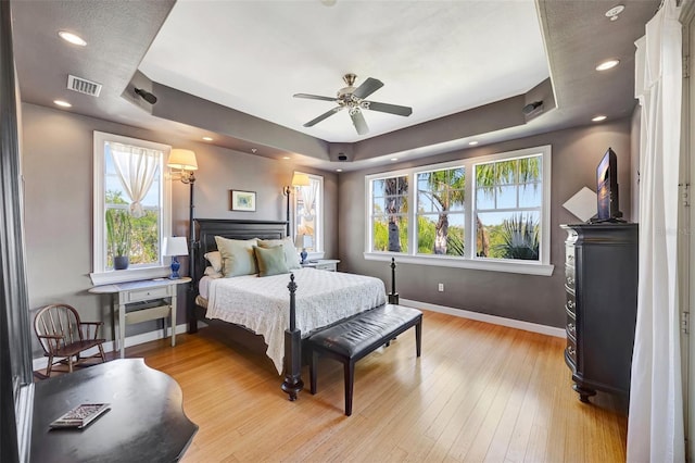 bedroom with a raised ceiling, baseboards, light wood finished floors, and multiple windows