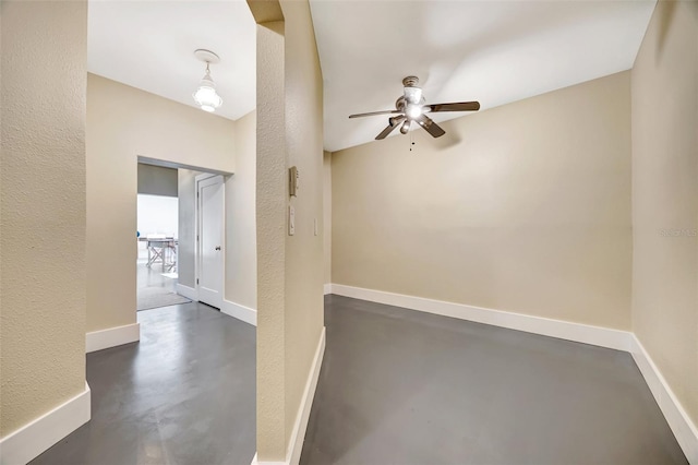 spare room with concrete flooring, a textured wall, a ceiling fan, and baseboards