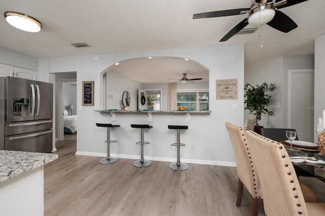 kitchen featuring a breakfast bar, stainless steel fridge with ice dispenser, arched walkways, and light wood finished floors