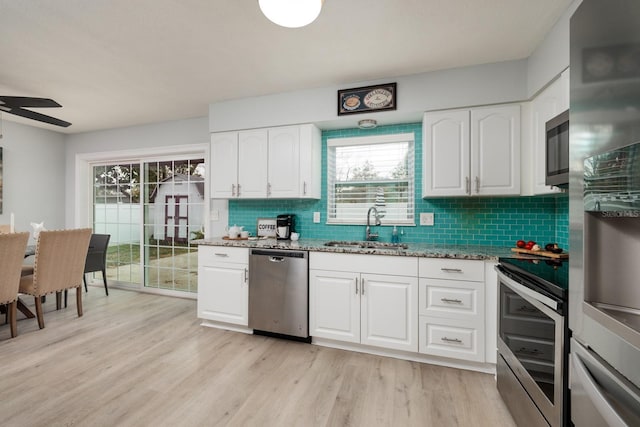 kitchen with light stone countertops, light wood-type flooring, decorative backsplash, appliances with stainless steel finishes, and a sink