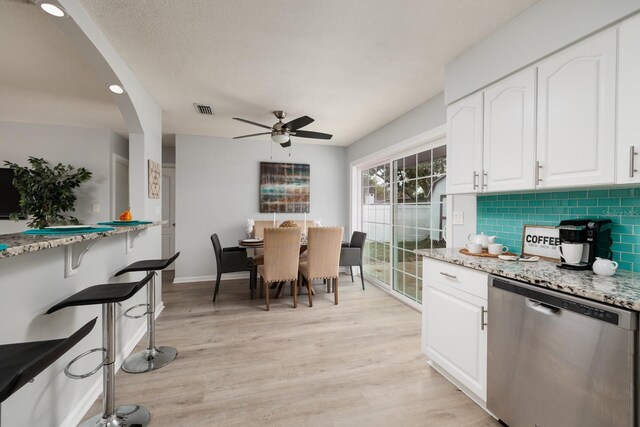 kitchen with light wood finished floors, backsplash, light stone countertops, dishwasher, and white cabinetry