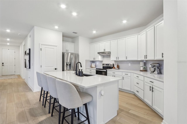 kitchen featuring stainless steel appliances, a sink, white cabinets, light countertops, and an island with sink