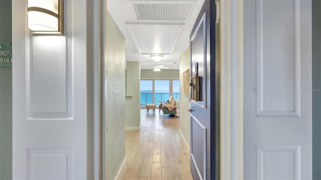 hall with attic access, visible vents, baseboards, a water view, and light wood-type flooring