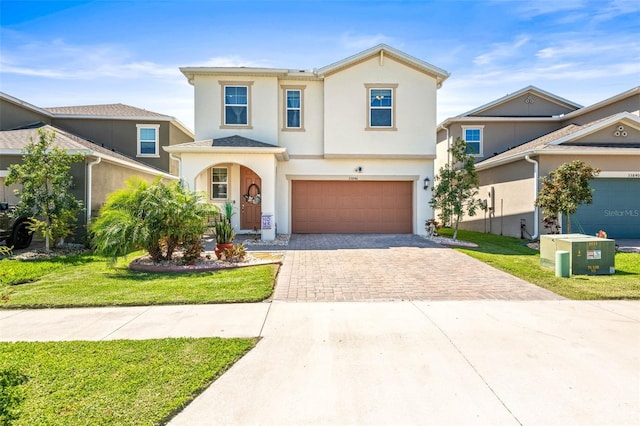 traditional-style house with decorative driveway, an attached garage, a front lawn, and stucco siding