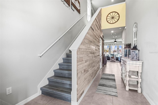 stairway with a ceiling fan, brick wall, a towering ceiling, an accent wall, and tile patterned floors