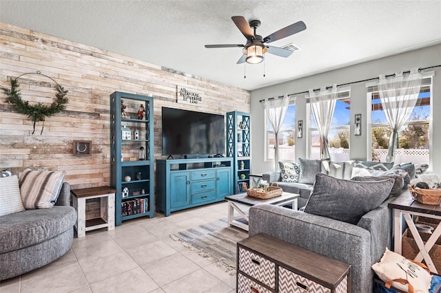 living area with wooden walls, light tile patterned floors, a ceiling fan, and a textured ceiling