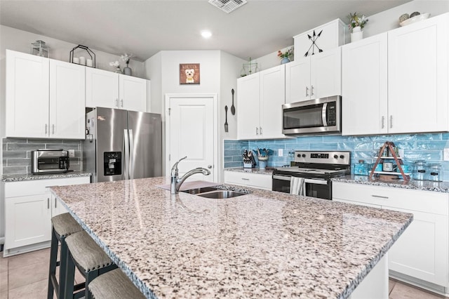 kitchen featuring light stone countertops, visible vents, a sink, stainless steel appliances, and tasteful backsplash